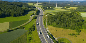 Aerial view of a highway cutting through a green landscape with wind turbines, showcasing sustainable logistics. - Supply Chain News