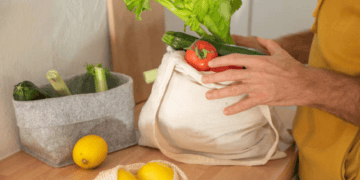 A man is exploring ethical sourcing by putting carefully selected vegetables into a tote bag.