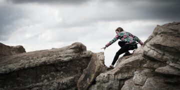 Woman reaching across a rocky gap. A challenging journey. - Supply Chain News