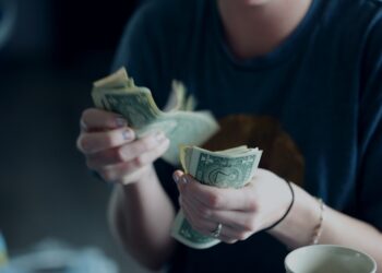 Key stakeholders observe as a woman presents a stack of money in front of a cup, highlighting the importance of anti-money laundering training.