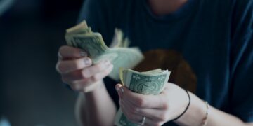 Key stakeholders observe as a woman presents a stack of money in front of a cup, highlighting the importance of anti-money laundering training.