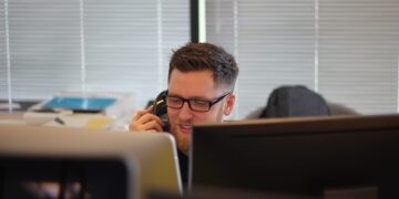 A man strengthening Congressional leadership while talking on a phone in front of a computer.