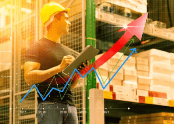 A man in a hard hat is holding a clipboard in a warehouse, where he closely monitors market growth and trends.