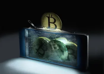 A phone with a bitcoin sitting on top of it, emphasizing its connection to the UK Investment Manager.