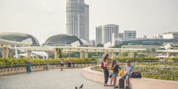 A group of people sitting on a bench in front of an expanding skyscraper in Singapore, discussing anti-money laundering measures and the ownership of luxury assets.