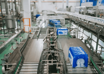 A conveyor belt in a factory with sustainable FMCG packaging trends featuring blue bottles on it.