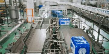 A conveyor belt in a factory with sustainable FMCG packaging trends featuring blue bottles on it.