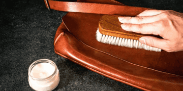 A person is gently brushing a luxury leather bag.