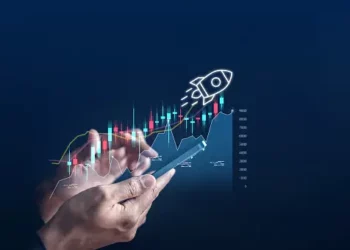 Hands using a smartphone displaying an upward trending graph with a rocket launching, symbolizing growth and success. - Supply Chain News