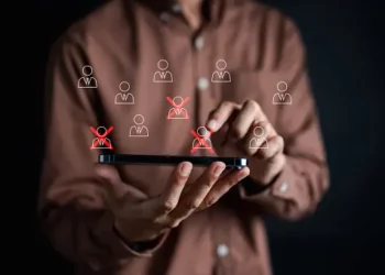 Person using smartphone to manage employee roster, highlighting layoffs with red X's. CSR program impact. - Supply Chain News