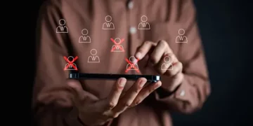 Person using smartphone to manage employee roster, highlighting layoffs with red X's. CSR program impact. - Supply Chain News