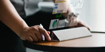 Person using tablet displaying graphs and data visualizations related to social impact and Microsoft Submittable partnership. - Supply Chain News