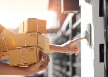 Delivery person ringing doorbell, holding stack of eco-friendly cardboard boxes. Greener deliveries. - Supply Chain News