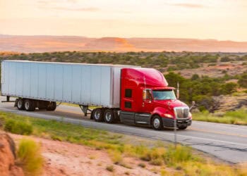 Red semi-truck hauling a large trailer on a highway. Trucking industry technology. - Supply Chain News