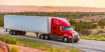 Red semi-truck hauling a large trailer on a highway. Trucking industry technology. - Supply Chain News