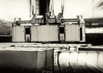 Cargo crane lifting shipping containers at a port, illustrating supply chain dynamics. - Supply Chain News