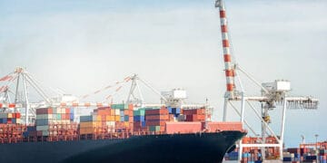 Container ship at port, cargo cranes loading containers. Maritime import volumes dip. - Supply Chain News