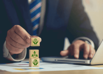 Person placing a block labeled "Environmental" atop blocks reading "Social" and "Governance," illustrating ESG principles. - Supply Chain News