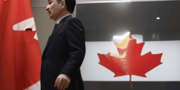 A man in a suit walking in front of the Canadian flag during an investigation on Uighur forced labor in Canada.