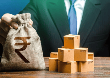 Businessperson holding a money bag with the Indian Rupee symbol, alongside a stack of cardboard boxes. - Supply Chain News