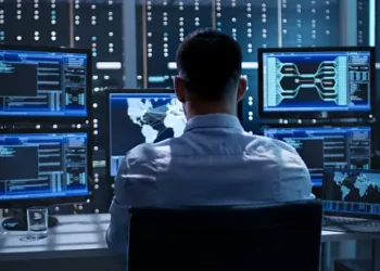 Cybersecurity analyst monitoring multiple screens displaying network data, illustrating a cybersecurity mesh architecture. - Supply Chain News