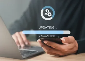 Person using laptop and phone, 80% update progress bar shown. Cybersecurity update in progress. - Supply Chain News