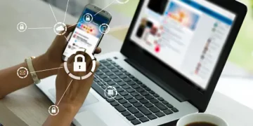 Person using laptop and phone, cybersecurity icons displayed. Homeland Security awareness. - Supply Chain News