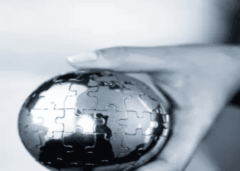 Hand holding a metal puzzle globe representing global climate change challenges and solutions for COP28. - Supply Chain News