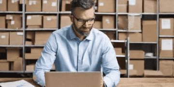 Man using laptop in warehouse, improving supply chain efficiency. - Supply Chain News