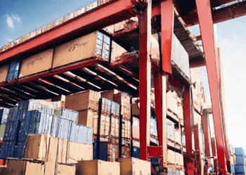 An expansive warehouse facility equipped with numerous boxes and a crane, providing an ideal solution for fourth party logistics.