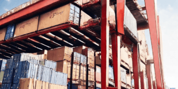 An expansive warehouse facility equipped with numerous boxes and a crane, providing an ideal solution for fourth party logistics.