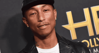A man in a leather jacket and hat, holding a Louis Vuitton Millionaire Speedy Bag, is standing on a red carpet.