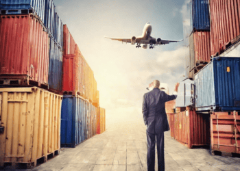 Businessman watching airplane landing near stacked cargo containers. Global supply chain data. - Supply Chain News