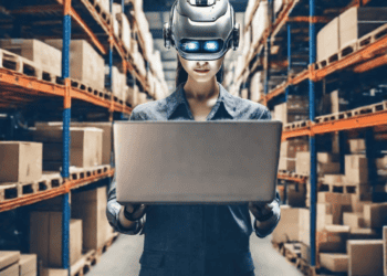 Woman in AI headset using laptop in warehouse, illustrating AI's impact on supply chain management. - Supply Chain News