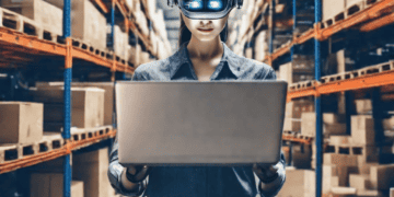 Woman in AI headset using laptop in warehouse, illustrating AI's impact on supply chain management. - Supply Chain News