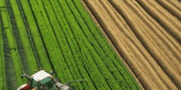 Aerial view of a tractor working a green field next to a harvested, brown field. Sustainable agriculture. - Supply Chain News