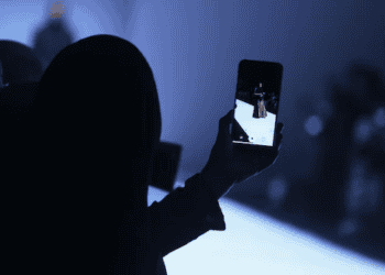 Person using smartphone to photograph a fashion show, showcasing the evolution of luxury brands towards accessibility. - Supply Chain News