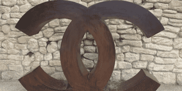 Large rusted metal Chanel logo in front of a stone wall. - Supply Chain News