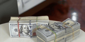 A stack of money on a table next to a bed, suggesting possession of counterfeit luxury items.