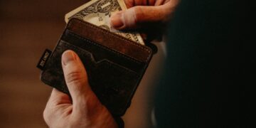 Close-up of hands holding a brown leather wallet and a one dollar bill. - Supply Chain News