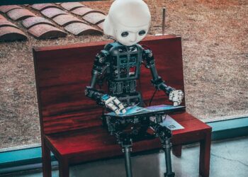 AI robot sitting on a bench, using a laptop. AI100 progress report. - Supply Chain News