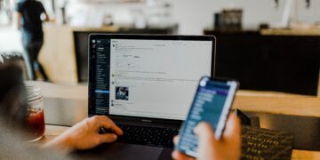 Person working on laptop and phone, reviewing KYC compliance data. - Supply Chain News