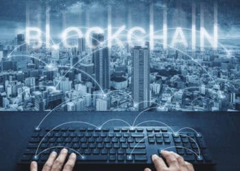 Hands typing on keyboard, "Blockchain" displayed over city skyline. Addressing supply chain disruptions. - Supply Chain News