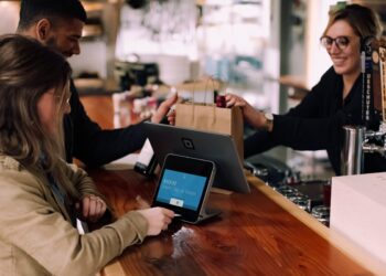Couple making a contactless payment at a point-of-sale terminal. The screen displays "$103.92 Insert, Tap, or Swipe. - Supply Chain News