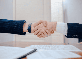 Businesspeople shaking hands, signifying a successful deal like the Authentic Brands Group's acquisition of Vince Holdings IP. - Supply Chain News