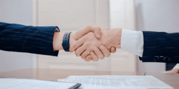 Businesspeople shaking hands, signifying a successful deal like the Authentic Brands Group's acquisition of Vince Holdings IP. - Supply Chain News