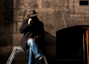 Man in hat sits on a stepladder, appearing suspicious. FBI warning about peer-to-peer payment scams. - Supply Chain News