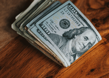 Stack of one hundred dollar bills on wooden table. Sales tax increase. - Supply Chain News