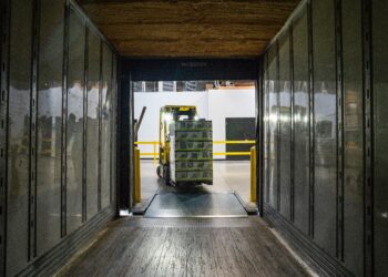 A forklift, used by logistics companies, is driving down a hallway in a warehouse.