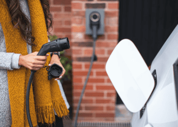 A woman is charging her electric car in front of a brick wall as part of the Lotus EV Venture.
